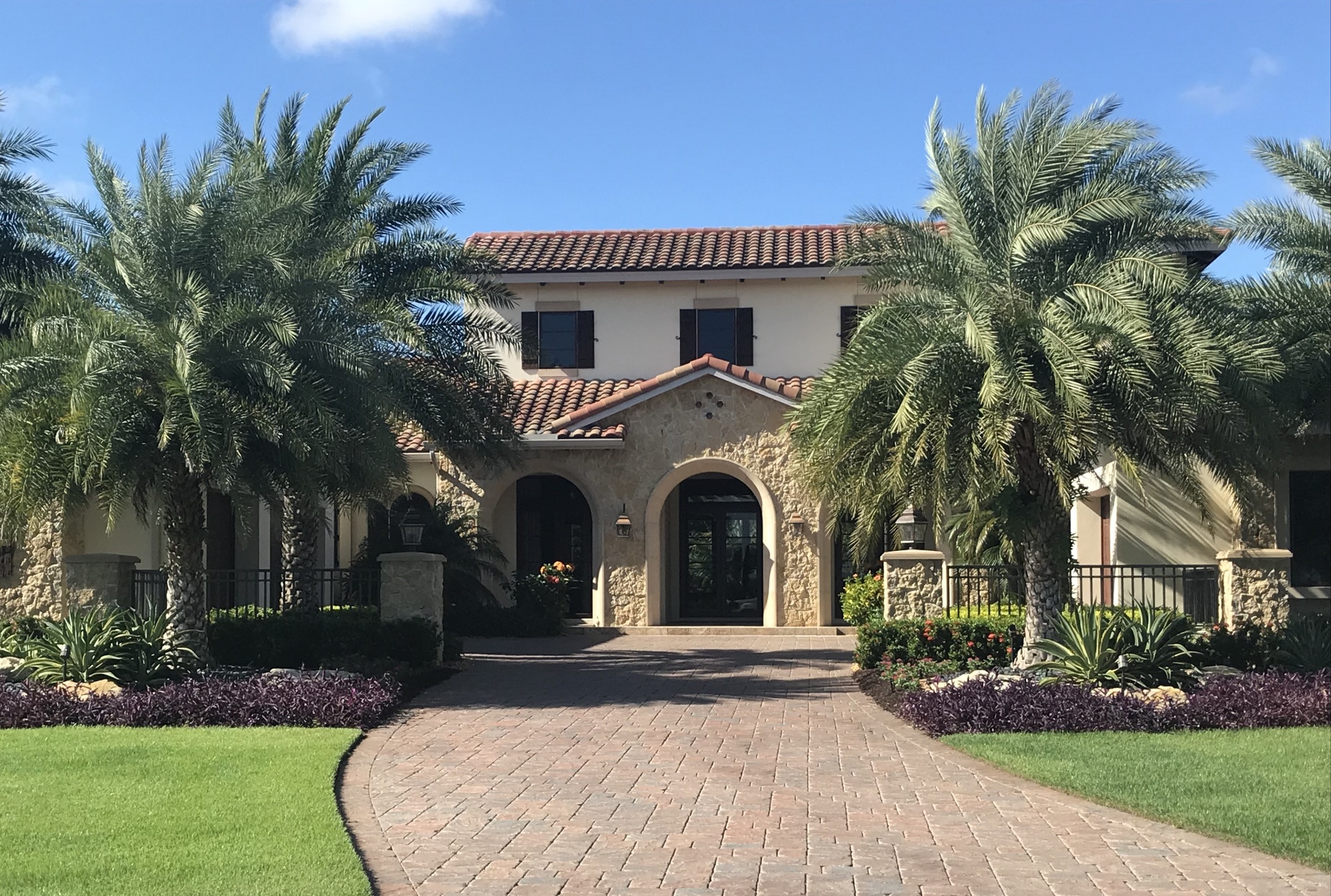 Stone-clad arched entry with date palms and bordered driveway at a private Florida residence